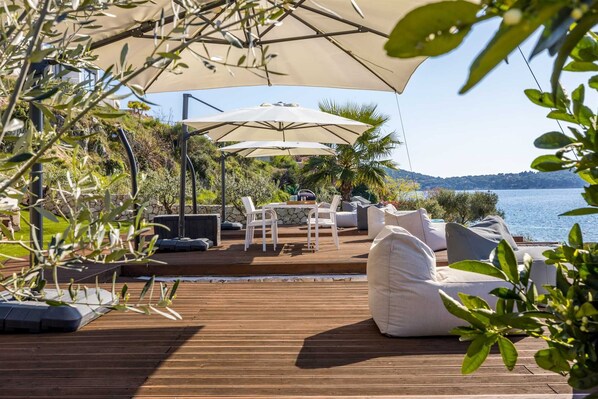 Une terrasse extérieure avec un plancher en bois, des meubles blancs et un grand parasol pour créer de l’ombre.