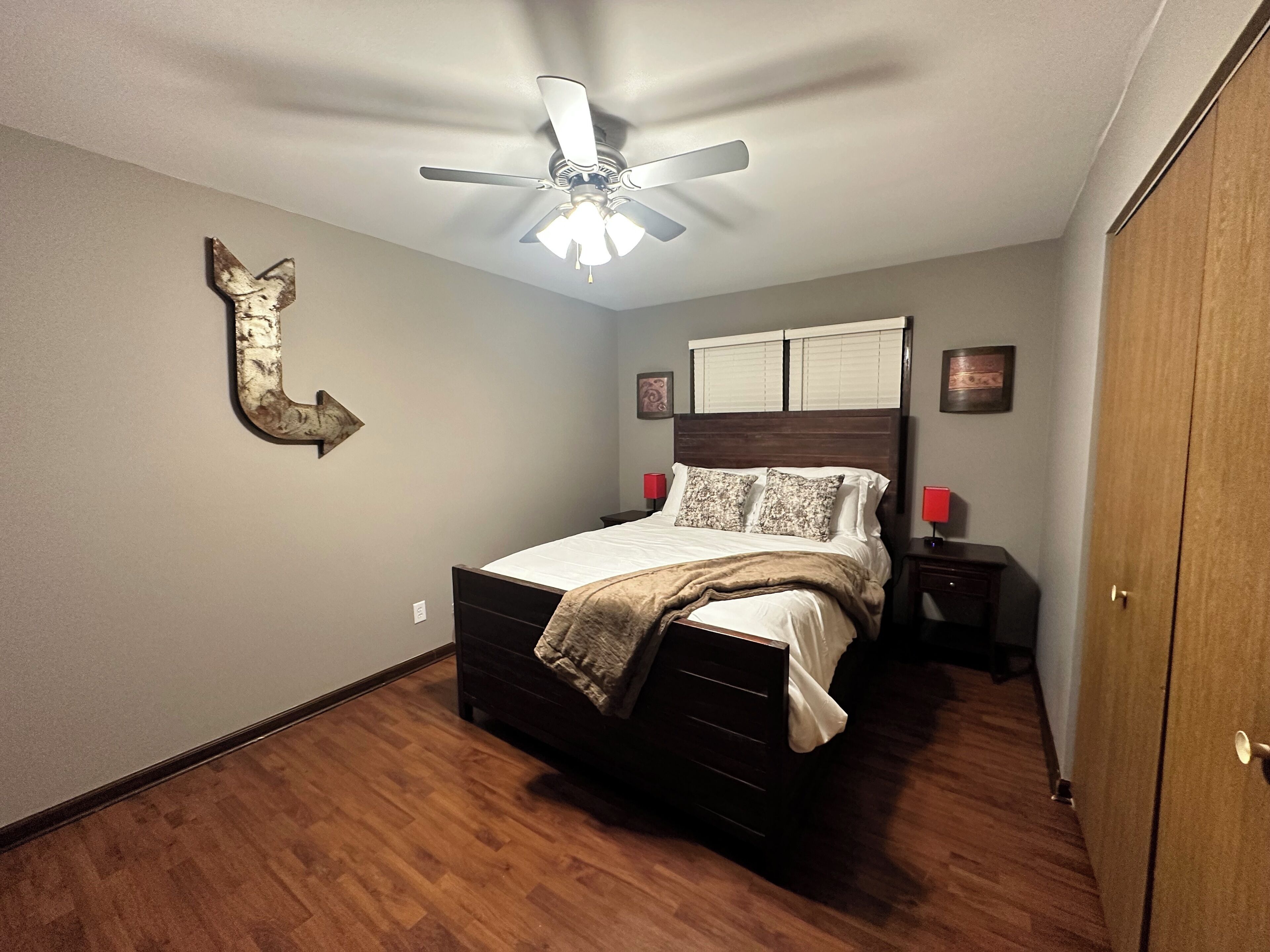 Un dormitorio con cama, ventilador de techo, suelo de madera y armario.