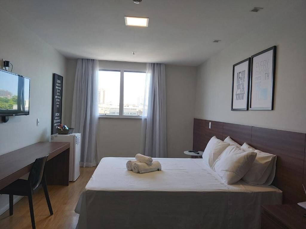 Una habitación de hotel con cama, escritorio, televisor y ventana con cortinas.