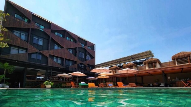 Ett modernt hotell med en swimmingpool, utomhusplats och en byggnad med halmtak.