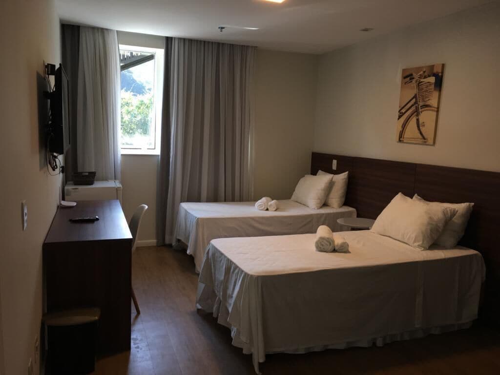 A hotel room with two beds, a desk, a chair, and a window with curtains.