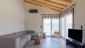 A modern living room with a sectional sofa, two wooden tables, a TV on a black stand, and large windows with sheer curtains. - Elegant house with Private Pool (Schinias)