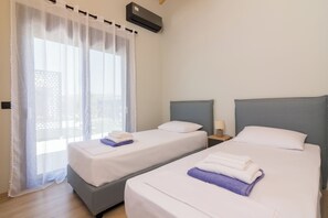 Two single beds with neatly folded towels, a nightstand, and a window with sheer curtains.