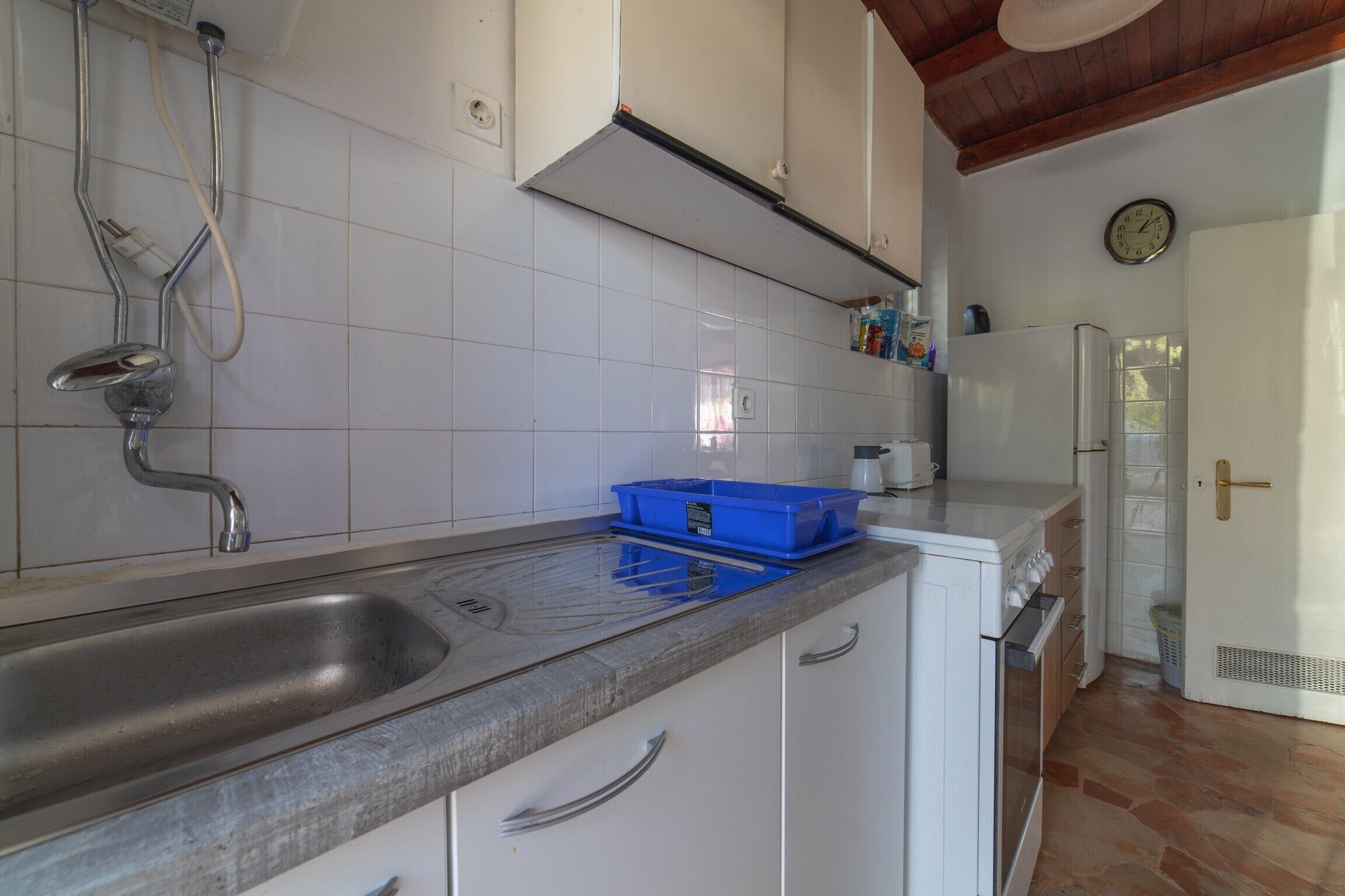 A kitchen with a sink, a blue container, white cabinets, and a white refrigerator.