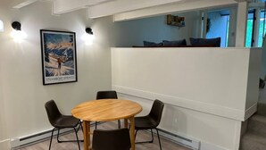 Ruokailutilassa on pyöreä puinen pöytä ja neljä tuolia, seinällä on kehystetty taulu ja tilan toisessa päässä on valkoinen sermi.