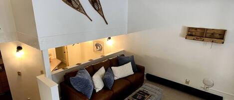 A modern living room with a brown leather sofa, a white armchair, and a patterned ottoman.