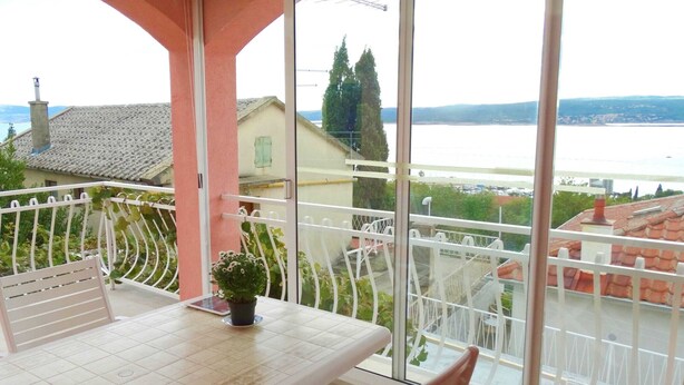 Un balcon avec une table et des chaises, une plante en pot et une vue sur une étendue d’eau et des bâtiments.