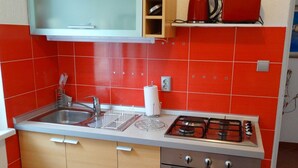 Une cuisine compacte équipée d’un évier, d’une cuisinière et d’un four, avec des carreaux rouges et des meubles en bois.
