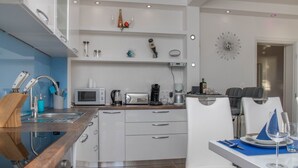 A modern kitchen with a built-in microwave, toaster, and coffee maker. There is a dining area with a white table and chairs, and a small decorative item on the wall. - Three Bedroom Apartment with Balcony and Sea View (Crikvenica)