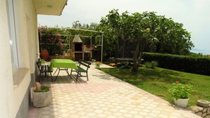 Eine Terrasse im Freien mit Tisch und Stühlen, einem Pflasterweg und einem Rasen mit Baum und Topfpflanzen.