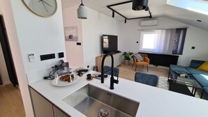 A modern kitchen with a stainless steel sink, a dining area with a glass table, and a living room with a sofa and a TV. - Two Bedroom Apartment with Balcony and Sea View (Crikvenica)