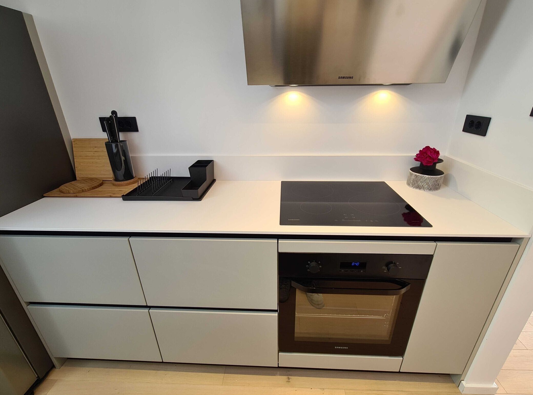 A modern kitchen with a built-in oven, a stainless steel range hood, and a minimalist countertop.