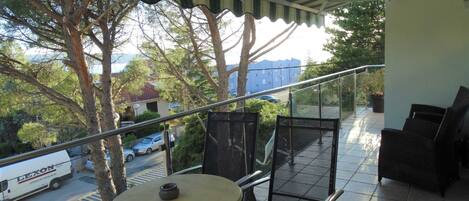 A balcony with a table and chairs, overlooking a street with parked cars and trees.