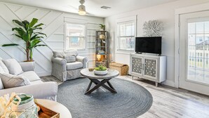En moderne stue med et rundt sofabord, grå sofaer, en stor plante, et fjernsyn og en reol.