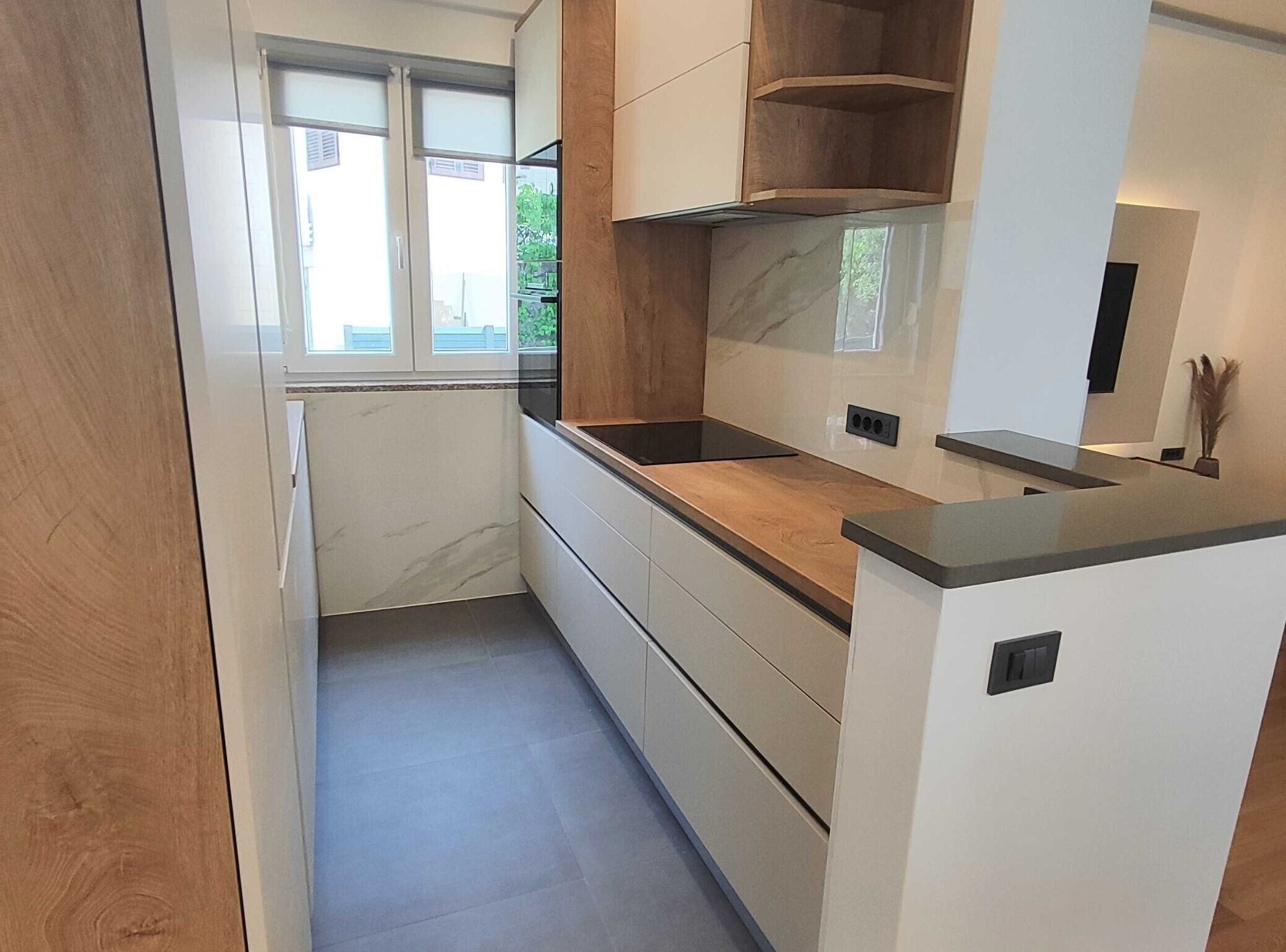 A modern kitchen with a wooden countertop, white cabinets, and a window providing natural light.