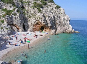 Una spiaggia con acque turchesi cristalline, scogliere rocciose e persone che prendono il sole e nuotano.