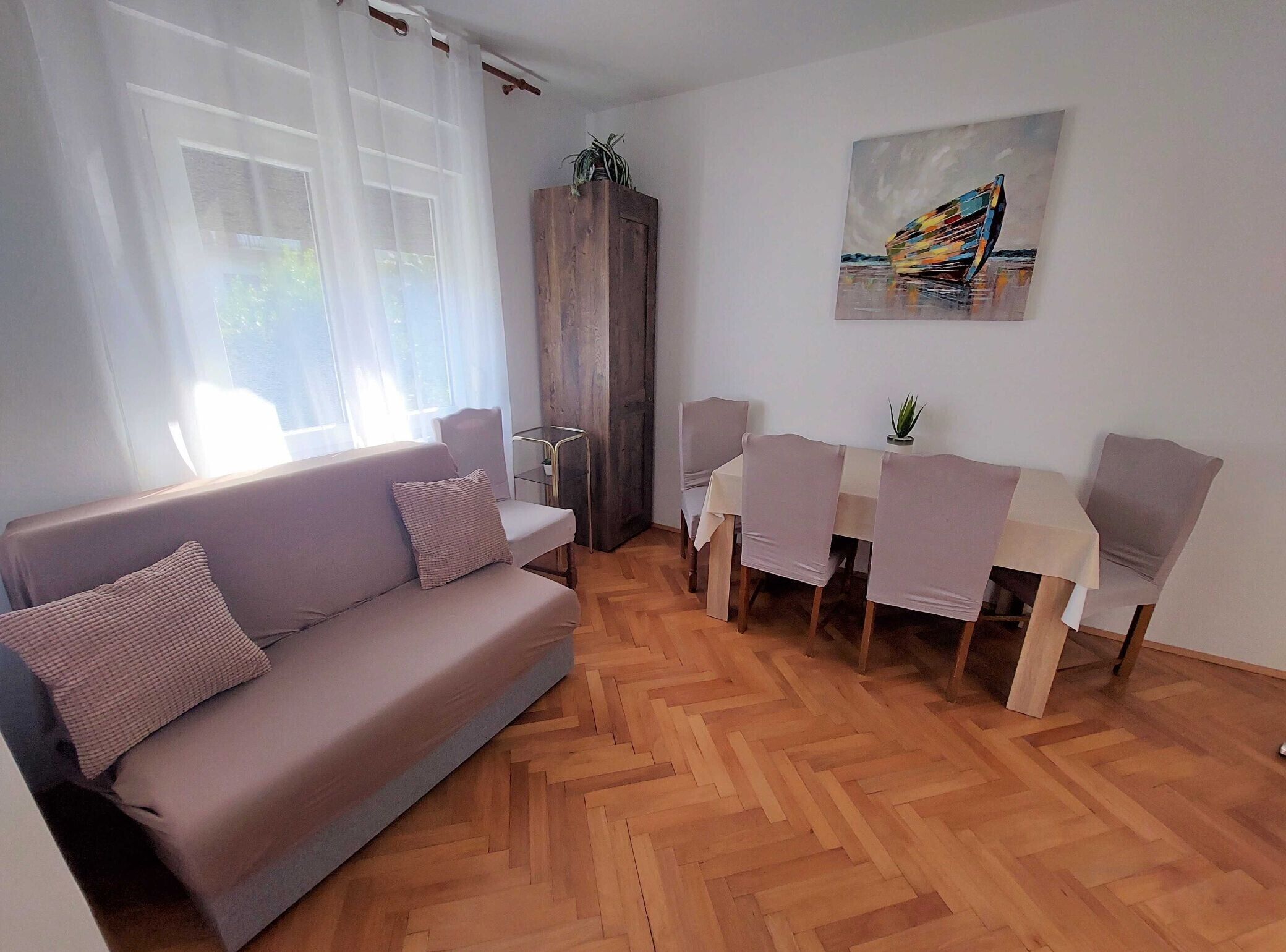 Un salon avec un canapé, une table à manger et des chaises, un meuble en bois et un tableau accroché au mur.