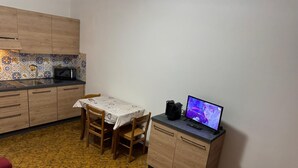 A compact kitchen with wooden cabinets, a tiled backsplash, a dining table with chairs, and a television on a counter. - Holiday home Alpine Serenity  (Aosta)