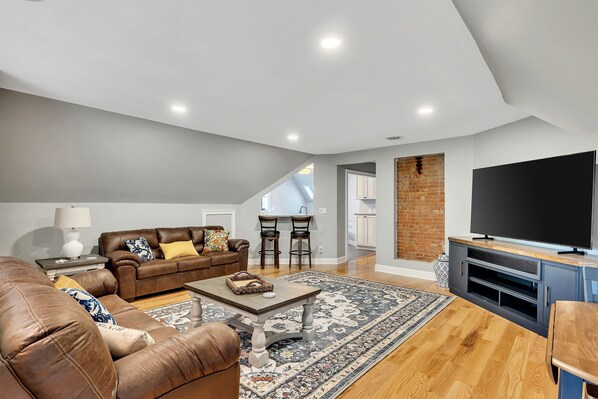 A spacious living room with a brown leather sofa, a coffee table, and a large flat-screen TV.