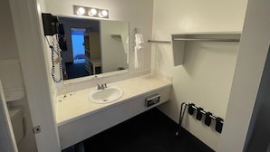 Ein Badezimmer mit einem weißen Waschbecken, einem beleuchteten Spiegel, einem Handtuchhalter und einer Duschkabine.