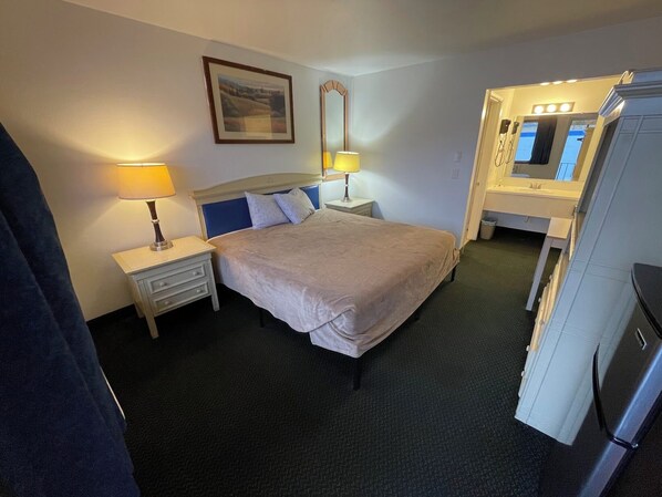A hotel room with a bed, bedside lamps, a mirror, a small table, and a refrigerator. - Canyon Inn (Lewiston)
