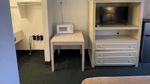 Ein Hotelzimmer mit einem Bett, einem kleinen Tisch mit einer Mikrowelle, einem Fernseher auf einem Schrank und einer Minibar.