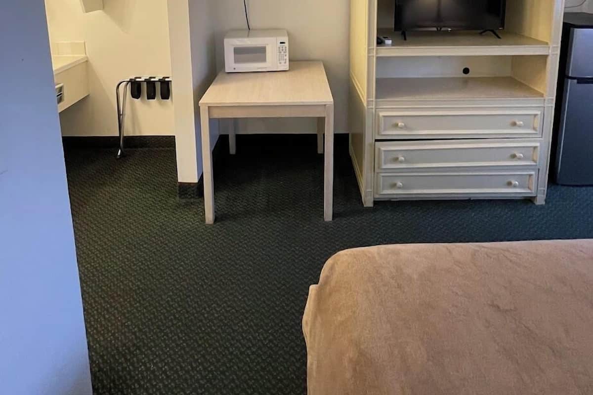 A hotel room with a bed, a small table with a microwave, a TV on a stand, and a minibar.