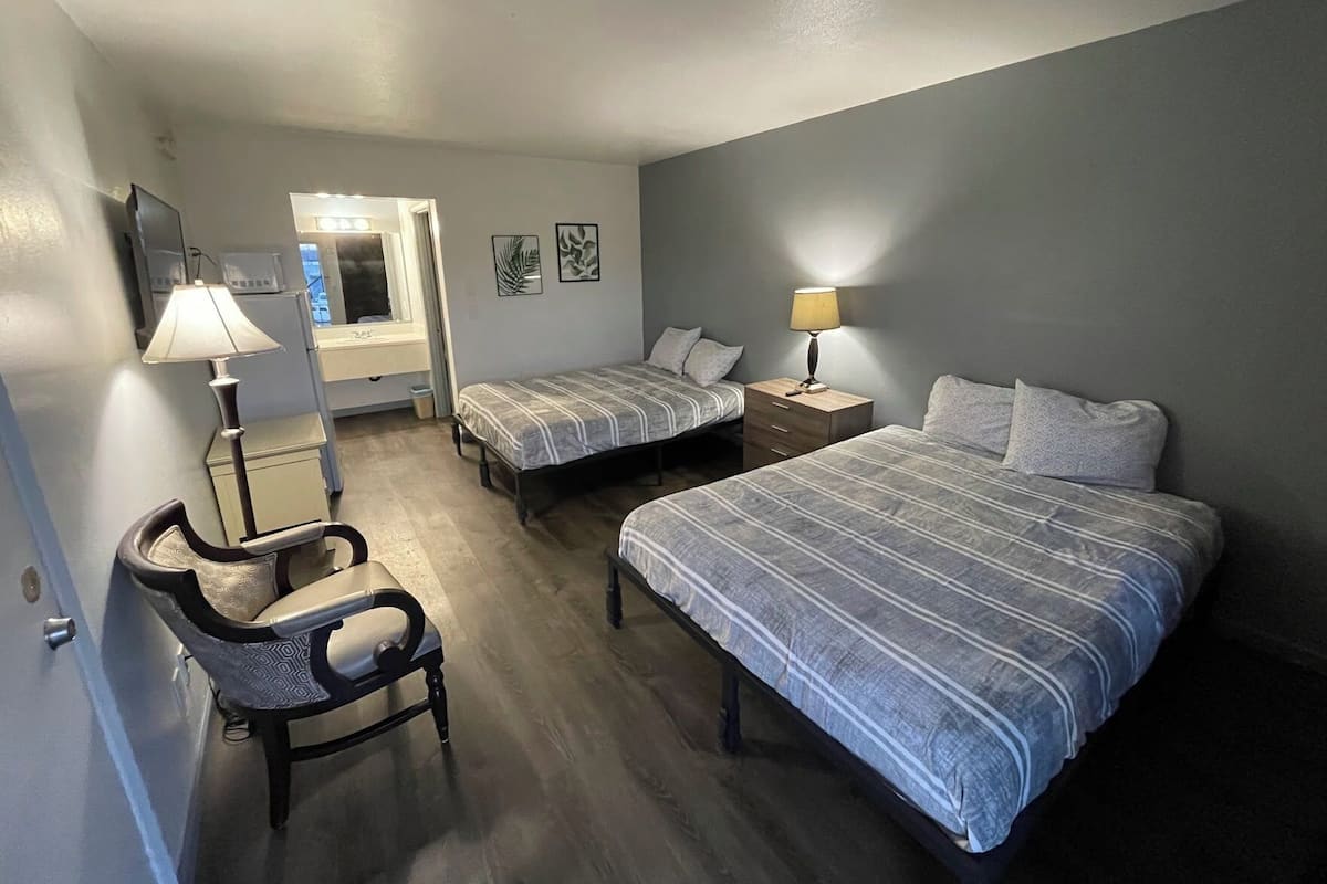 A bedroom with two beds, a chair, a desk, and a lamp.