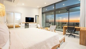 Ein modernes Hotelzimmer mit einem großen Bett, einem Schreibtisch mit Computer, einem Fernseher und einem großen Fenster mit Blick auf die Stadt.