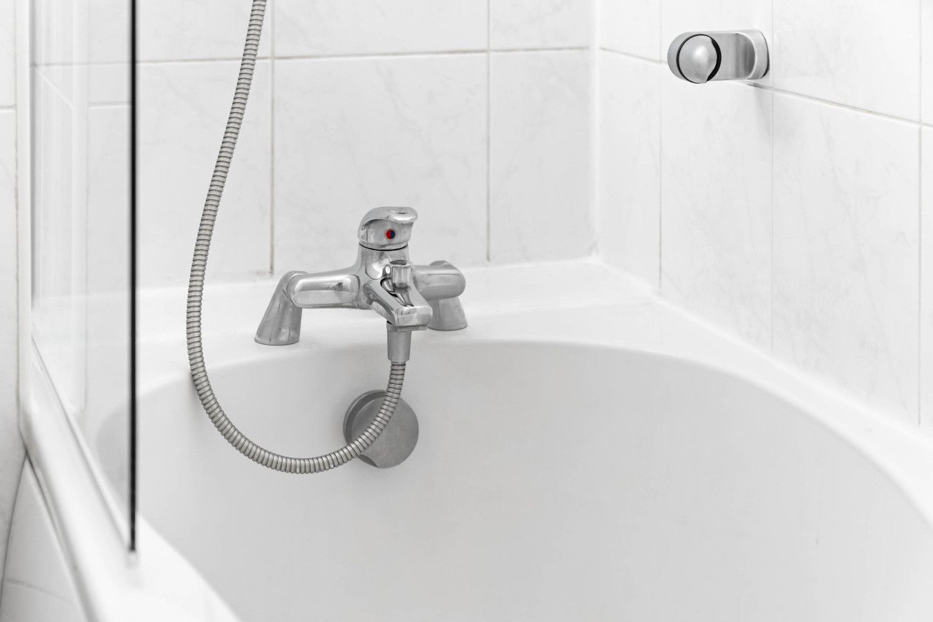 Een wit bad met een handdouche en een wandmengkraan.