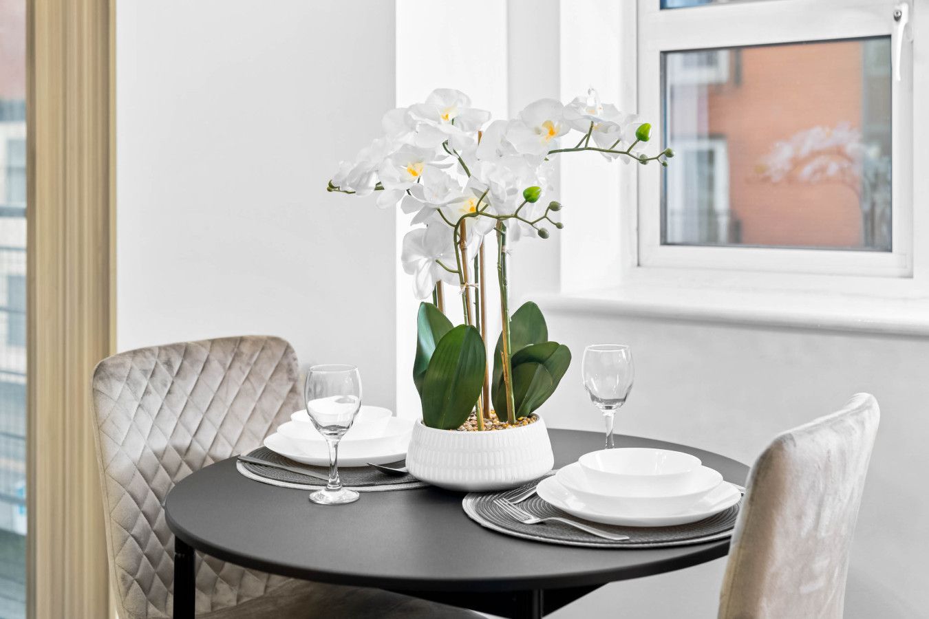 Ein Esstisch mit weißen Tellern, zwei Weingläsern und einer weißen Orchideenvase.