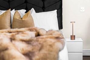 Una cama con cabecera negra, almohadas blancas y manta marrón.