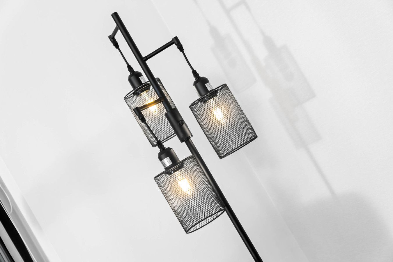 A modern black metal wall-mounted light fixture with three rectangular sections, each with a mesh cover and a visible light bulb.