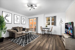 A modern living room with a sofa, coffee table, and TV. There is a dining area with chairs and a table.