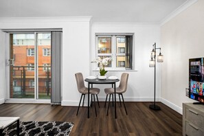 Un comedor moderno con una mesa dispuesta para dos, una planta en maceta y vistas de un edificio de ladrillo rojo a través de un gran ventanal corredizo.