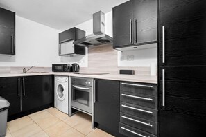 Una cocina moderna con armarios oscuros, electrodomésticos de acero inoxidable y suelo de baldosas.