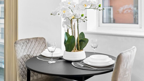Uma mesa de jantar com pratos brancos, duas taças de vinho e um vaso com orquídea branca.