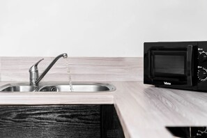 Una cocina con un lavamanos de acero inoxidable y un microondas negro.