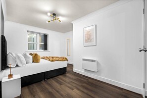 Un dormitorio con cama, ventana, radiador y puerta.