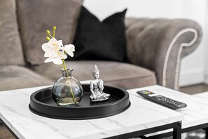 Una mesa de café de mármol con un jarrón de flores blancas, una estatua de Buda y un control remoto.