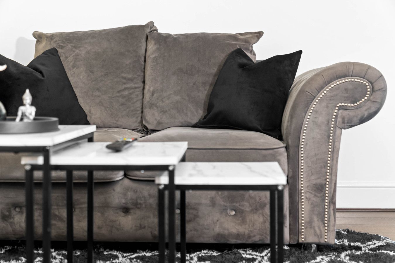 A grey sofa with black cushions, a small table with a remote control, and a black and white rug.