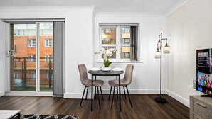 Un comedor moderno con una mesa dispuesta para dos, una planta en maceta y vistas de un edificio de ladrillo rojo a través de un gran ventanal corredizo.