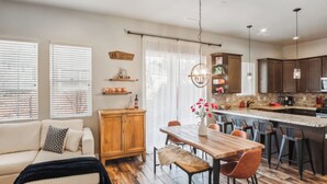 Una cocina moderna con una mesa de comedor de madera, taburetes de bar y una lámpara colgante.