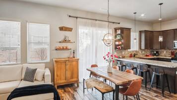 Une cuisine moderne avec une table à manger en bois, des tabourets de bar et un luminaire suspendu.