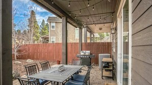 Un patio al aire libre con un espacio de estar cubierto, una parrilla y una mesa con sillas.