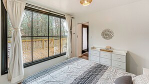A bedroom with a large window, a bed with patterned bedding, a bedside table, and a wall-mounted mirror. - Walk to Fox Lake: Pet-Friendly A-Frame w/ Fire Pit (Twin Lake)