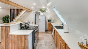 A modern kitchen with a central island, built-in appliances, and a wooden staircase. - Walk to Fox Lake: Pet-Friendly A-Frame w/ Fire Pit (Twin Lake)