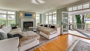 A spacious living room with a fireplace, large windows, and a balcony with a view of the outdoors. - Groton Home < 1 Mi to Beach on Long Island Sound! (Groton)