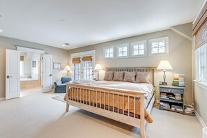 A bedroom with a wooden bed, a nightstand with books, a chair, and a window with blinds. - Walk to DU, Dining & Parks: Spacious Denver Home! (Denver)