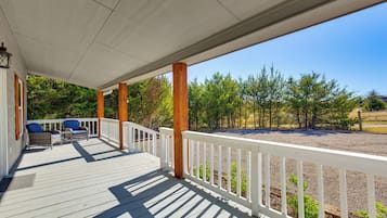A covered deck with white railings, wooden posts, and two blue chairs.